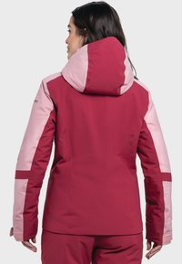Red and pink outerwear jacket with a hood, featuring contrasting paneling, smooth texture, and snug fit, designed for functional use.