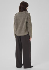Übergroßer, hellgrau-grüner Strickpullover mit geripptem Saum und Ärmeln. Kombiniert mit locker sitzenden schwarzen Hosen. Glatte Textur und entspannter Schnitt.