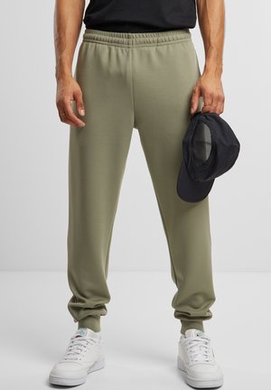 Jogging en tricot de couleur vert olive avec une taille élastique, des poignets effilés et des poches latérales. Associé à des baskets blanches et une casquette noire.