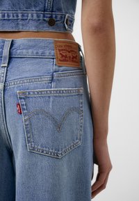 Světle modré džíny z denimu s koženou nášivkou Levi's a výrazným křivkovým stehem na zadních kapsách, se malou červenou etiketou.