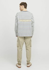 Gestreiftes Langarmshirt in Weiß und Marineblau, mit einem Textgrafik in Creme auf dem Rücken. Kombiniert mit beigen Cargo-Hosen und Sneakern.