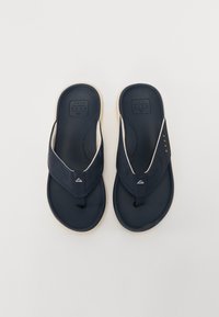 Marineblå flip-flops med en strukturert fotseng, stoffremmer og en lys såle, med en liten logo detalj på remmen.