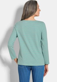 Grünes Langarmshirt mit horizontalen weißen Streifen, rundem Halsausschnitt und lässiger Passform. Kombiniert mit blauen Jeans für einen entspannten Look.