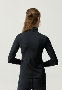 Top negro de manga larga con cuello alto, fabricado en un material suave y elástico. Presenta un diseño ajustado y detalles de costura sutiles, vista posterior mostrada.