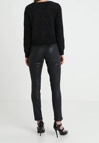 Musta, pörröinen neulepaita pitkine hihoineen, yhdistettynä istuviin mustiin nahkahousuihin ja korkokengillä, joissa on nilkkaremmit.