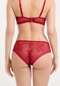 Ensemble de lingerie en dentelle rouge profond, avec motifs floraux et bords festonnés. Le soutien-gorge est doté de bretelles réglables et d'une fermeture à agrafes dans le dos.