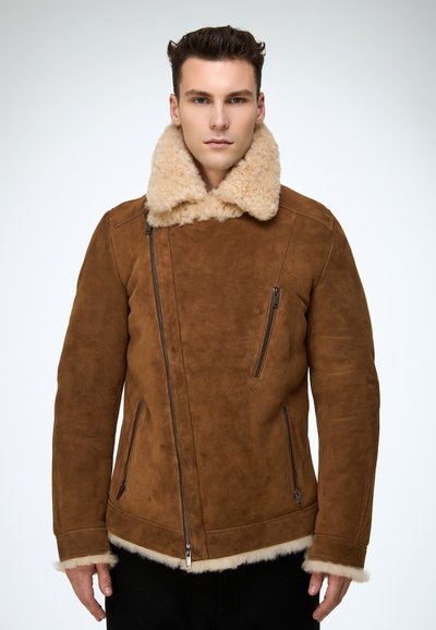 Braune Wildlederjacke mit großem, flauschigem beigem Kragen, asymmetrischem Reißverschluss, zwei Seitentaschen und einem Saum, der mit Lammfellbesatz verziert ist.