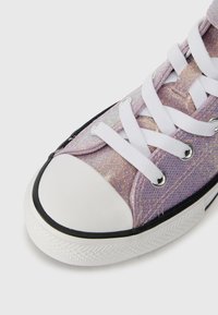 Fialové tenisky s třpytivým svrškem, bílými tkaničkami a bílou gumovou špičkou. Mají černé lemování a texturovanou podešev.