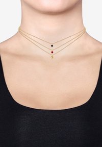 Guldtonad lagerhalsband med tre kedjor som pryder svarta, röda och gula cirkulära hängen som vilar på en bar hals.
