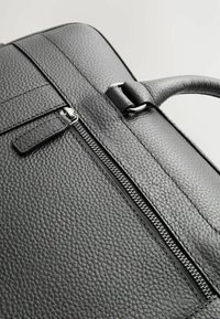 Black leather bag with a textured finish, featuring a zip closure and metallic hardware accents. Includes a top handle for carrying.