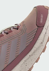 Helle rosa Laufschuhe aus strukturiertem Stoff, mit grauen Streifen und einer gemusterten Gummisohle. Auffälliges "RAIN RDY" Etikett an der Seite.