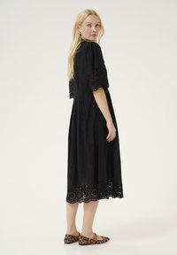 Black embroidered dress with short puff sleeves, laser-cut floral hem, cinched waist, and lightweight fabric; paired with leopard print flats.
