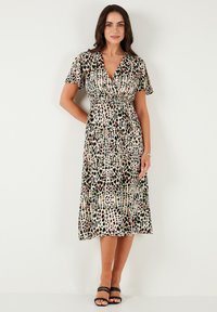 Leopard print dress in lightweight fabric, wrap design, short flutter sleeves, mid-calf length, complemented by black strappy sandals.