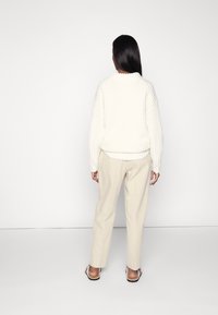 Dikke witte geribbelde gebreide trui met een hoge kraag, gecombineerd met beige rechte broek en simpele sandalen, gezien vanuit de achterkant.