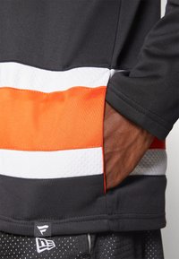 Juodas sportinis marškinėlis su horizontaliomis baltomis ir oranžinėmis juostelėmis, turintis tekstūruotų panelių. Apima siūlomi kraštai ir prekės ženklas apačioje.