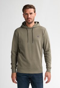 Sudadera verde oliva de manga larga, con capucha ajustable y un pequeño logo en el pecho. Textura suave, diseño ajustado, combinada con jeans azules.