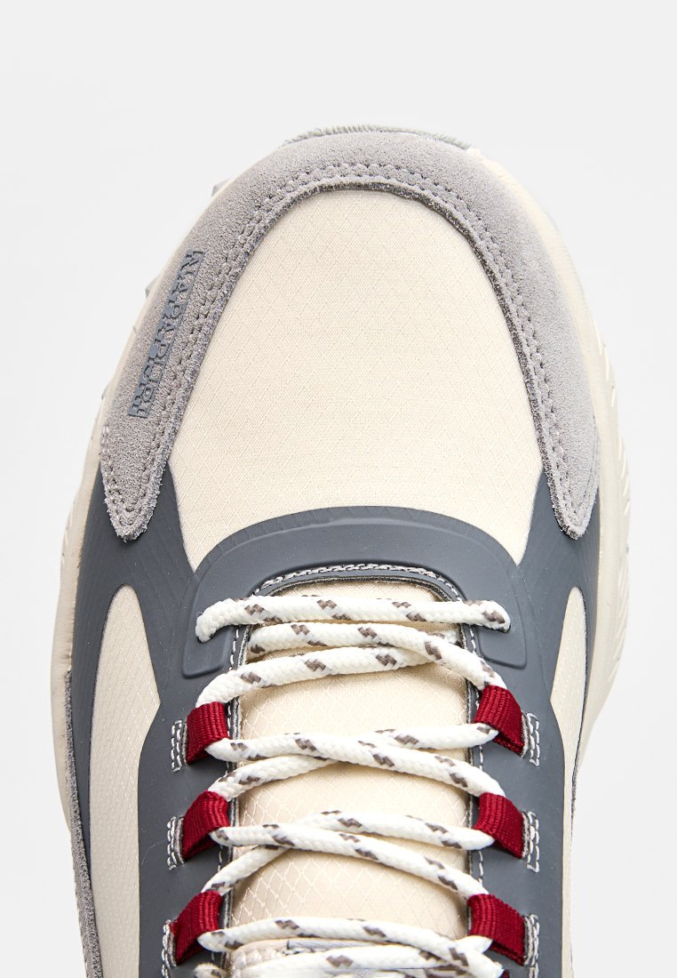 Baskets de sport beige clair avec accents gris, empeigne texturée et lacets rouges. Présentent un col rembourré et des détails à motifs sur les lacets.