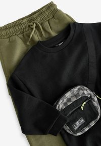 Svart sweatshirt med ett diagonalt mönster, tillsammans med olivgröna joggers med elastisk midja. Inkluderar en liten svart och grå rutad påse.