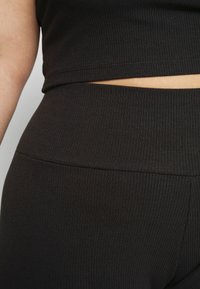 Černý žebrovaný krátký top v kombinaci s legínami s vysokým pasem. Látka působí texturovaně a elasticky, s čistým zakončením na švech.