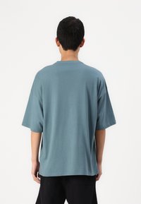 Laza szabású, rövid ujjú póló tompa teal színű pamutból. Egyszerű kerek nyakkivágással és letisztult varrásokkal rendelkezik.