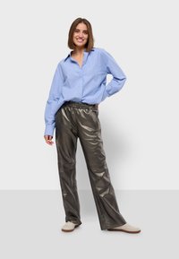 Gestreepte blauwe overhemd met knopen, ruime pasvorm; metallic zilveren, wijde broek; beige sneakers. Broek heeft een elastische tailleband.