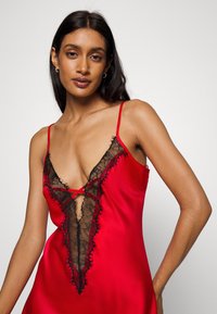 Red satin slip dress featuring a deep V lace trim and cutout design. Thin straps and lace detailing create a contrasting texture.
