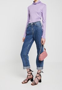 Top a maniche lunghe lilla, jeans in denim blu a vita alta, polsini arrotolati, tacchi neri con cinturini e una piccola borsa a tracolla rosa con una trama testurizzata.