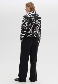 Camicia a maniche lunghe astratta in bianco e nero con motivo, abbinata a pantaloni neri larghi. Tessuto morbido con una vestibilità rilassata e polsini risvoltati.