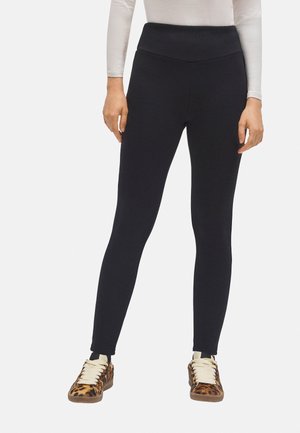 Leggings negros con una cintura alta, hechos de tela elástica, con una textura suave y un ajuste ceñido; combinados con zapatillas de deporte de estampado de leopardo marrón.