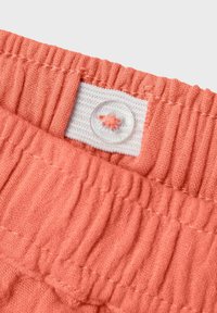 Tejido de color coral rosa con textura acanalada, con cinturilla elástica y un botón transparente en una etiqueta blanca.