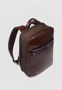 Zaino in pelle marrone con finitura liscia, caratterizzato da dettagli blu, doppio scomparto con cerniera e spallacci imbottiti regolabili.