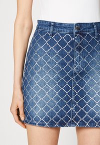 Gonna di jeans con dettagli di strass a forma di diamante, tessuto blu, design aderente, chiusura frontale con bottoni e orlo dritto.