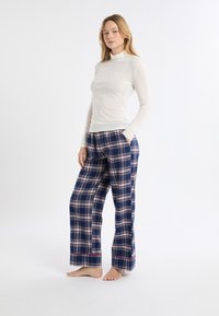 Langärmeliges cremefarbenes Oberteil und blaue Karopajamahose mit roten Akzenten; weicher Stoff, entspannte Passform und seitliche Taschen an der Hose.