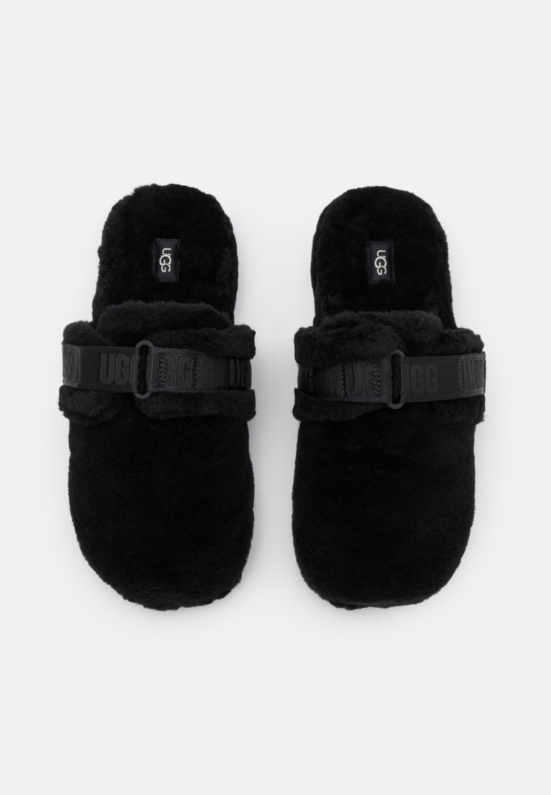 Schwarze, mit Fell gefütterte Rutsch-Slipper mit verstellbarem schwarzen Riemen, der das "UGG"-Logo trägt. Weiche Textur und ergonomische Form für zusätzlichen Komfort.