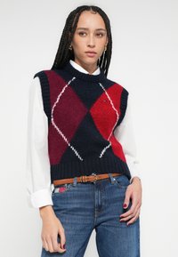 Pletená sveter bez rukávov s námorníckym modrým, červeným a bordovým škvrnitým vzorom, s rebrovaným výstrihom a priliehavým pásom.