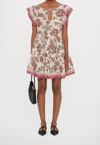 Robe à motifs floraux en crème avec des manches volantes, un col en trou de serrure et des accents rouges. Associée à un sac à main tissé noir et des ballerines noires.