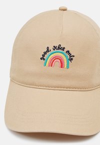 Beige Baseballcap mit gesticktem Regenbogenmotiv in Pastellfarben und dem Text "Good Vibes Only". Strukturierter Stoff mit gebogenem Schirm.