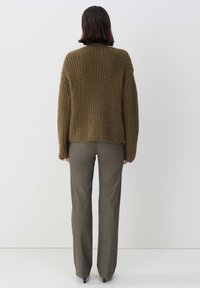 Olivgrön stickad tröja med lös passform och strukturerat mönster, kombinerad med tajta olivfärgade byxor och svarta klackskor.