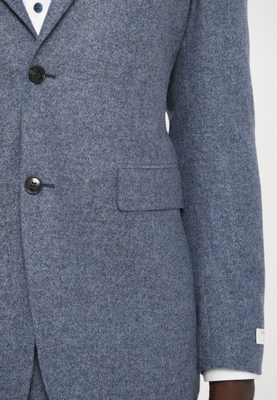 Houndstooth-patterned gray blazer made of textured fabric, featuring three buttons, a chest pocket, and a white cuff detail.