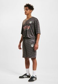 Grå sportssett med en løs kortermet skjorte og matchende shorts. Begge har et geometrisk mønster og merking i røde og svarte aksenter.