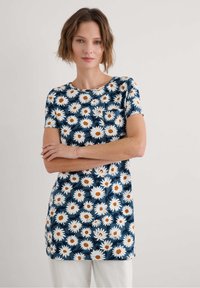 Gėlių tunika su tamsiai mėlynu fonu, papuošta baltais ramunėlių žiedais su oranžinėmis vidurkiu. Trumpomis rankovėmis, apvaliu kaklu ir minkšta medžiaga.