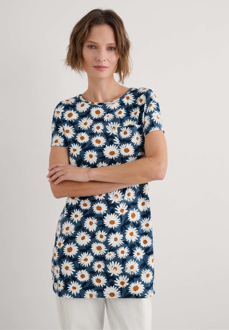 Gėlių tunika su tamsiai mėlynu fonu, papuošta baltais ramunėlių žiedais su oranžinėmis vidurkiu. Trumpomis rankovėmis, apvaliu kaklu ir minkšta medžiaga.