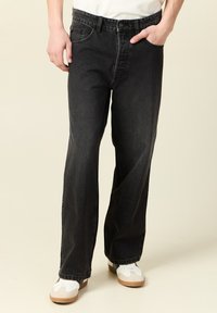 Svarta denimjeans med avslappnad passform, med knappgylf, bältesöglor och framfickor. Bärs med vita sneakers och en vanlig t-shirt.