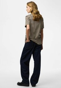 Prugasta majica smeđe i krem boje, izrađena od pamuka, uparena s širokim tamnoplavim trapericama i crnim cipelama.