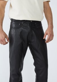 Schwarze Lederhosen mit glatter Textur, Fünf-Taschen-Design und Metallbeschlägen. Gerade geschnitten und mit einem Knopf- und Reißverschluss ausgestattet.