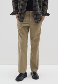 Pantaloni in corduroy color khaki con taglio dritto, dotati di chiusura a un bottone e tasche laterali, abbinati a scarpe nere.