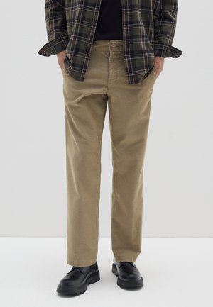 Pantalones de corduroy color caqui con corte recto, que cuentan con un cierre de un botón y bolsillos laterales, combinados con zapatos negros.