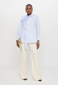 Ανοιχτό μπλε πουκάμισο με μεγάλη ανθισμένη διακόσμηση και ριγέ μπροστά, συνδυασμένο με λευκά παντελόνια με φαρδιά ποδόγυρο και γυαλιστερές μαύρες γόβες.