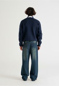 Marineblaues Sweatshirt mit überschnittenen Schultern, kombiniert mit lässigen Jeans im Loose-Fit-Stil, die ausgewaschene Akzente und zwei Gesäßtaschen mit Nähdetails aufweisen.