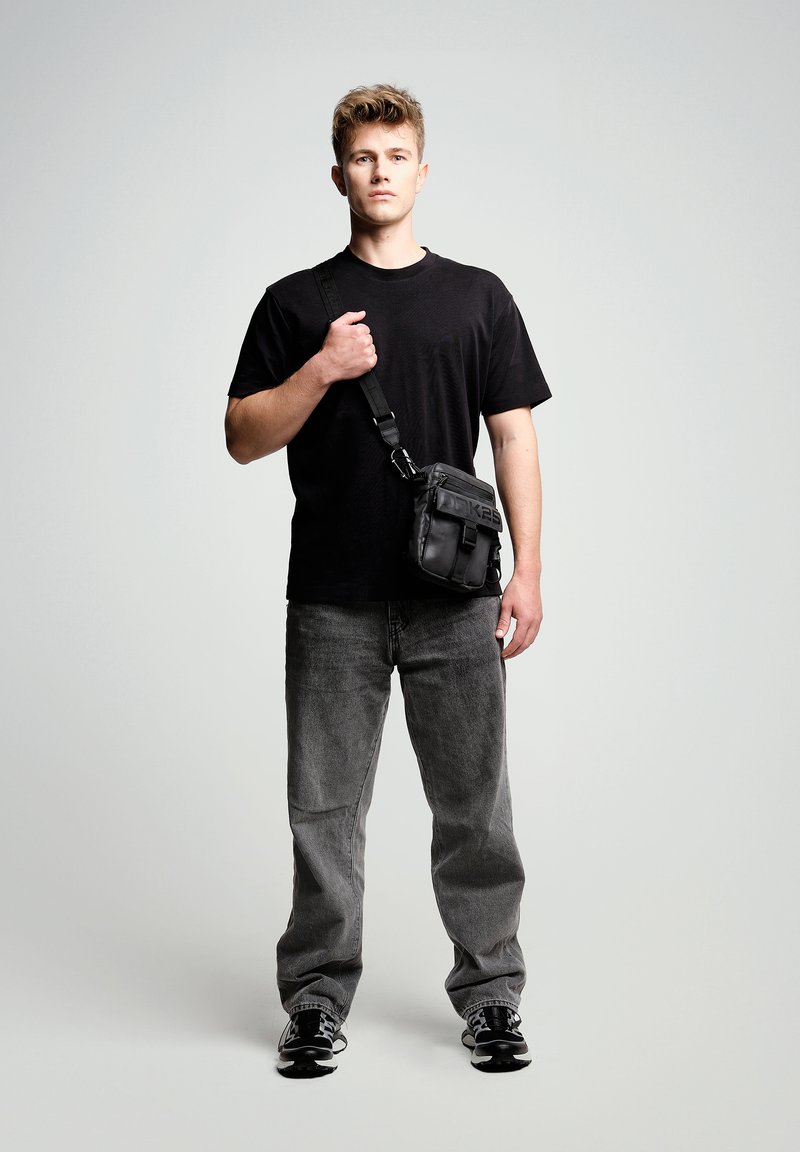 Black crossbody bag made from synthetic material, featuring a textured surface, adjustable strap, and front pocket with zipper.